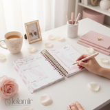 Person using a pink planner with a cup of tea and stationery on a desk, featuring the brand 'lolamir'.